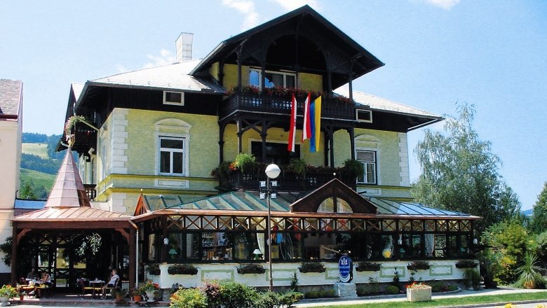 A traditional building with a glass veranda and Austrian flag, surrounded by plants.