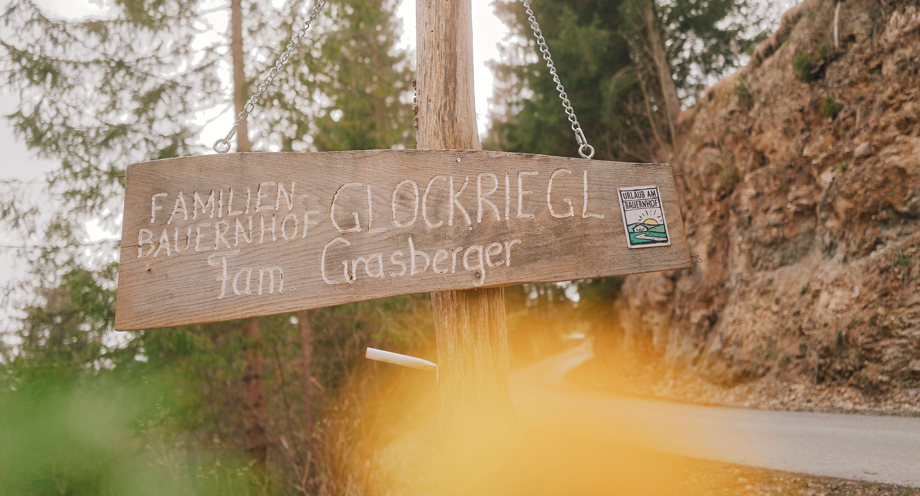 Wooden sign with the inscription 'Familienbauernhof Glockriegl Fam. Grasberger' on a forest path.