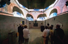 Visitors view a projection of a viaduct in a room with concrete walls.