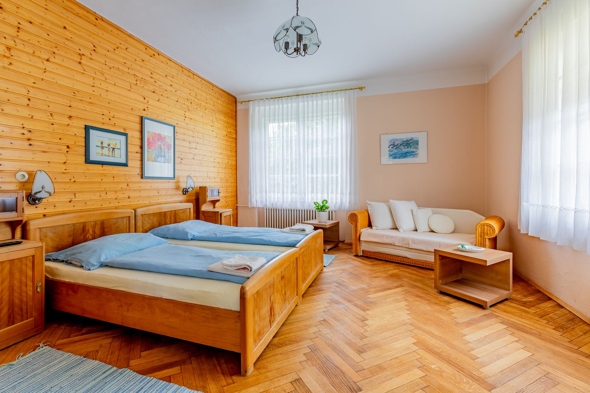 Cozy bedroom with wooden walls, two beds, sofa and wooden floor.
