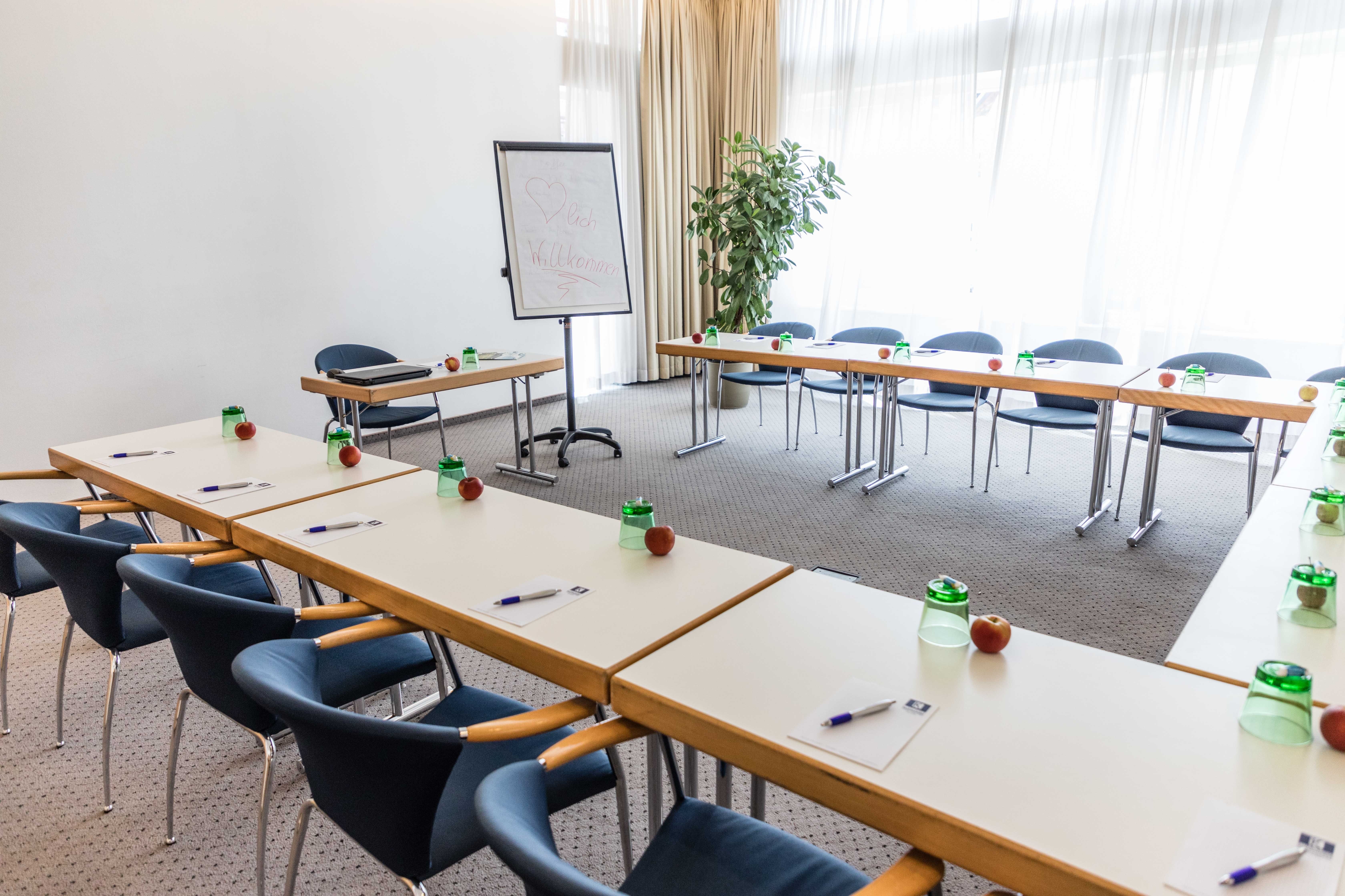 Conference room with U-shaped tables, chairs, flipchart and writing materials.