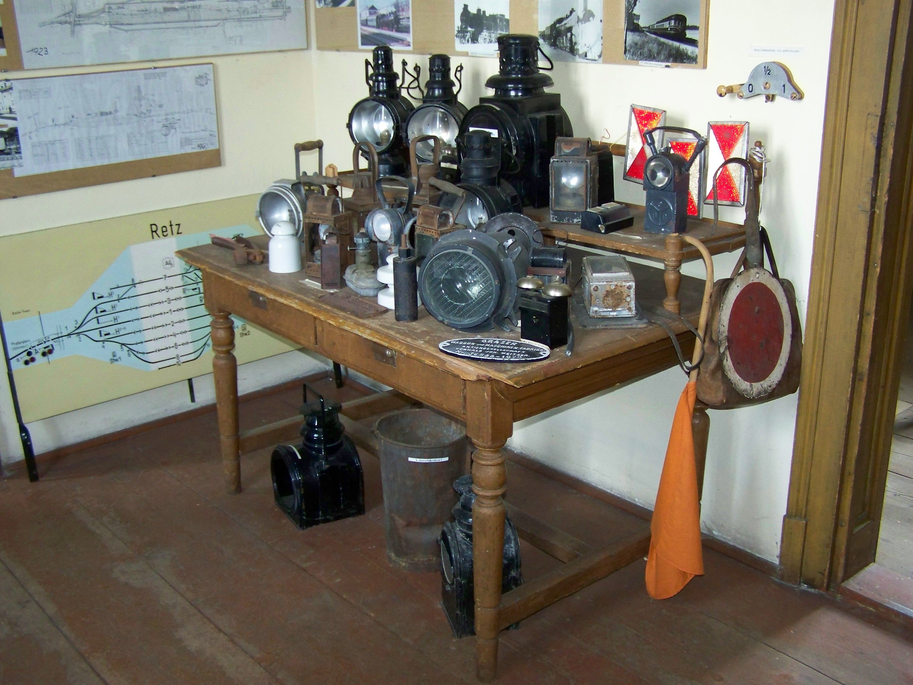 A table with old railroad lamps and signals in a room with historical plans on the wall.