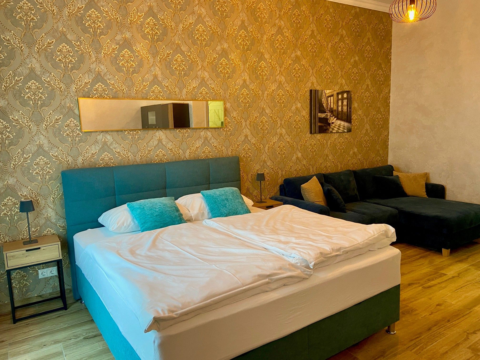 Elegant hotel room with double bed, blue couch and golden wallpaper.