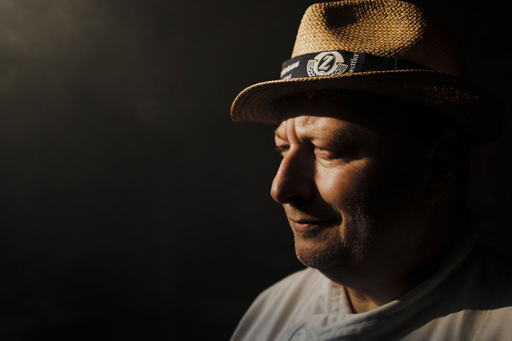 Portrait of a man with a straw hat in profile, standing in the shade.