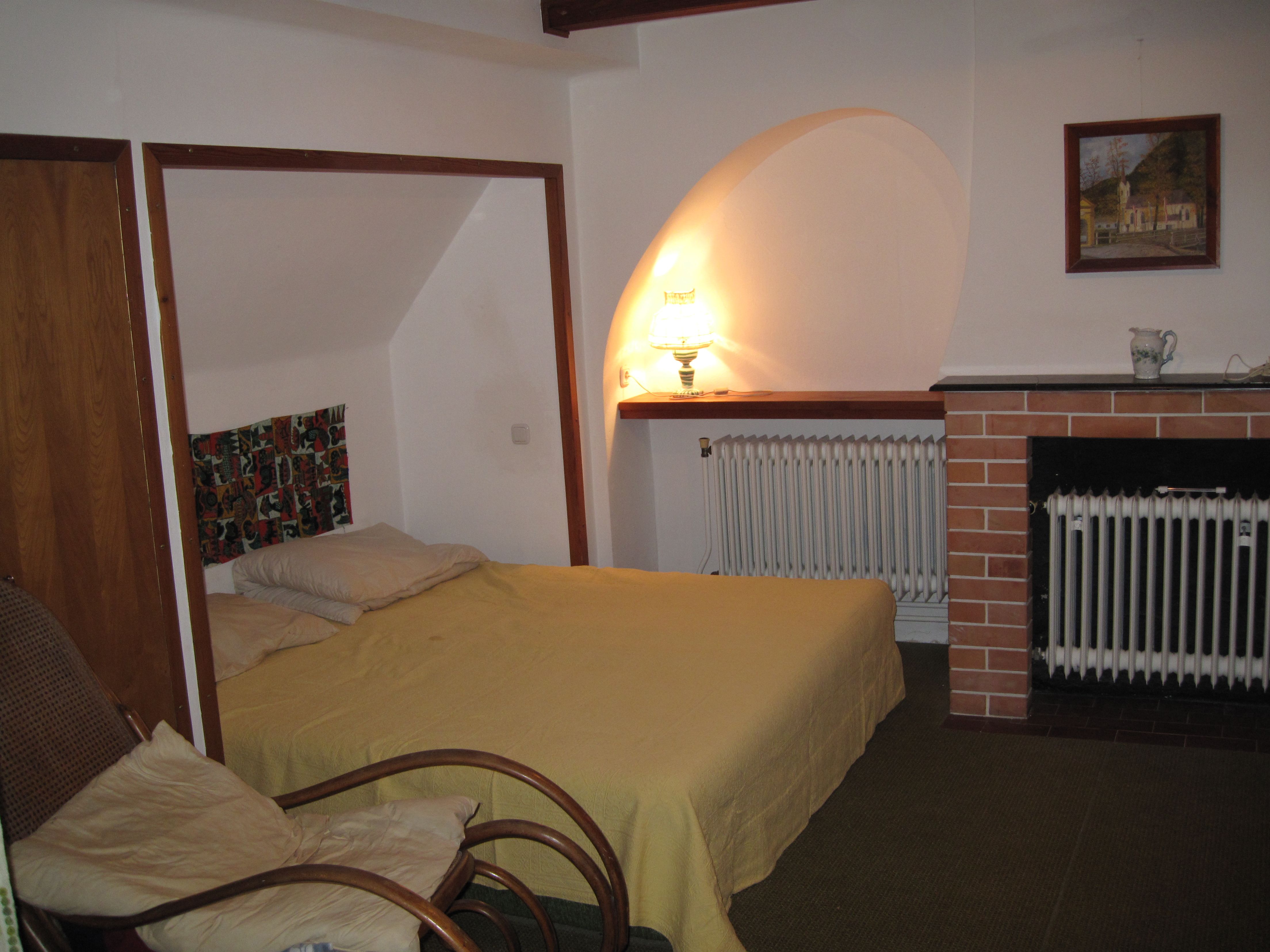 A cozy bedroom with a bed, an armchair, a lamp and a fireplace.