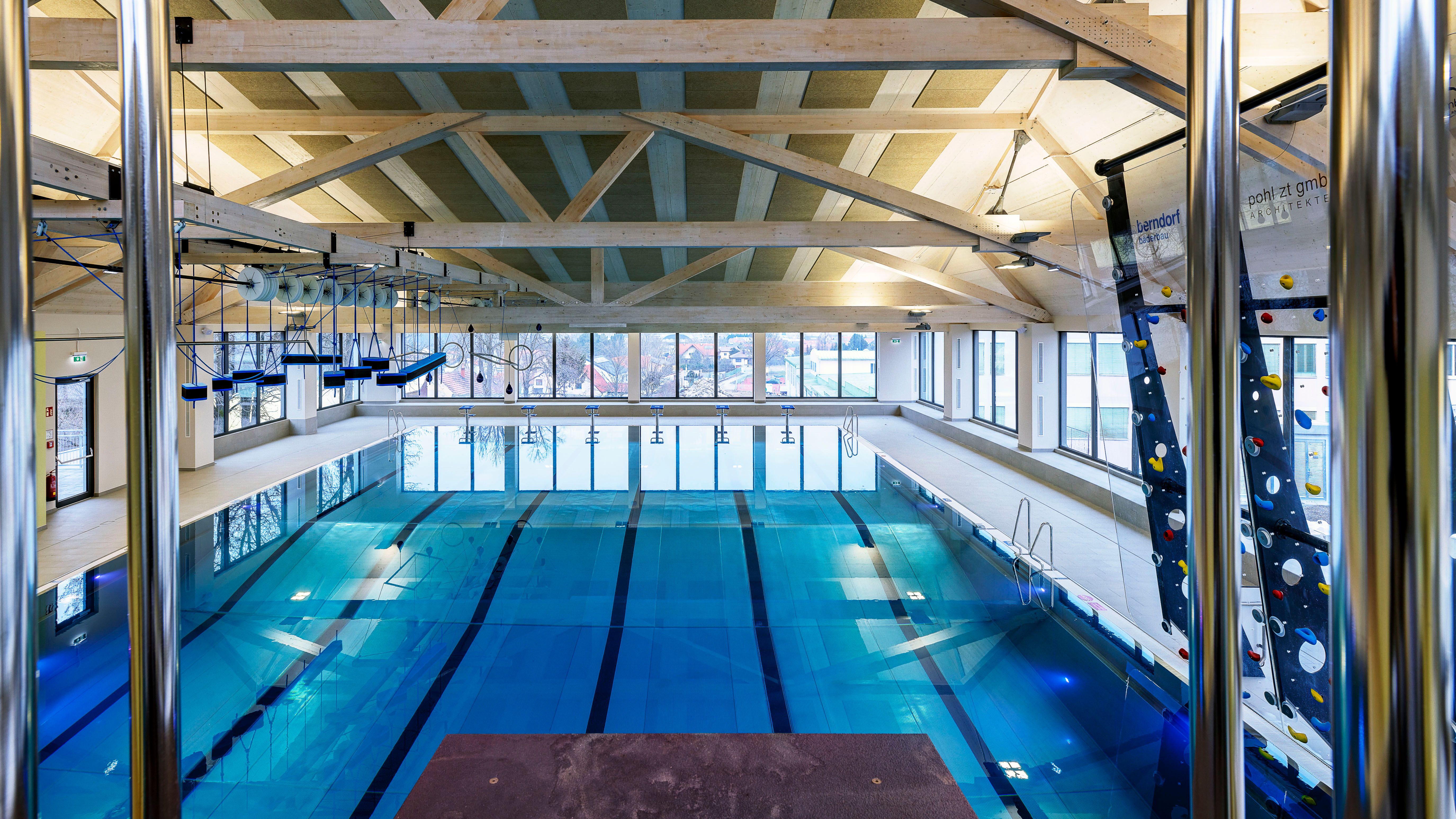 Interior view of a modern indoor pool with swimming lanes and climbing wall.