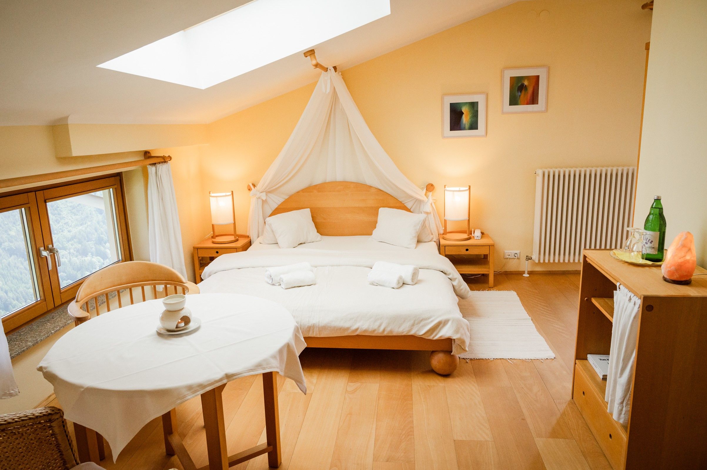 Cozy double room with wooden furniture, large bed, table and chairs, window with a view and soft lighting.