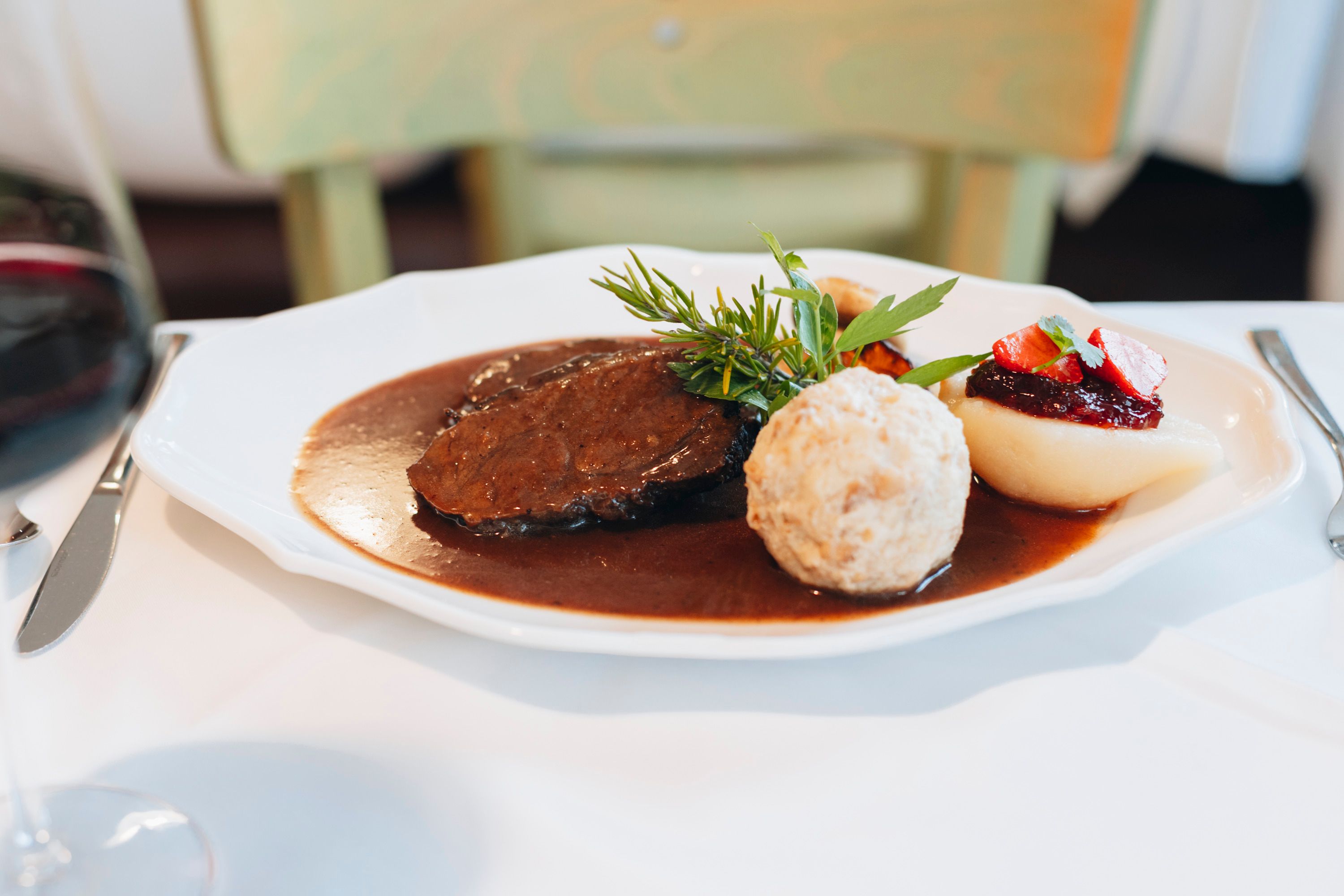 A plate with saddle of venison, bread dumplings, pear with cranberries and sauce, decorated with herbs.