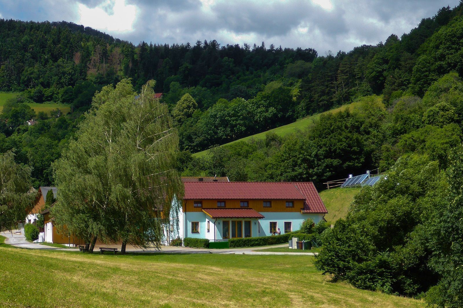 A vacation farm with red roofs in a green, hilly landscape with trees and meadows.