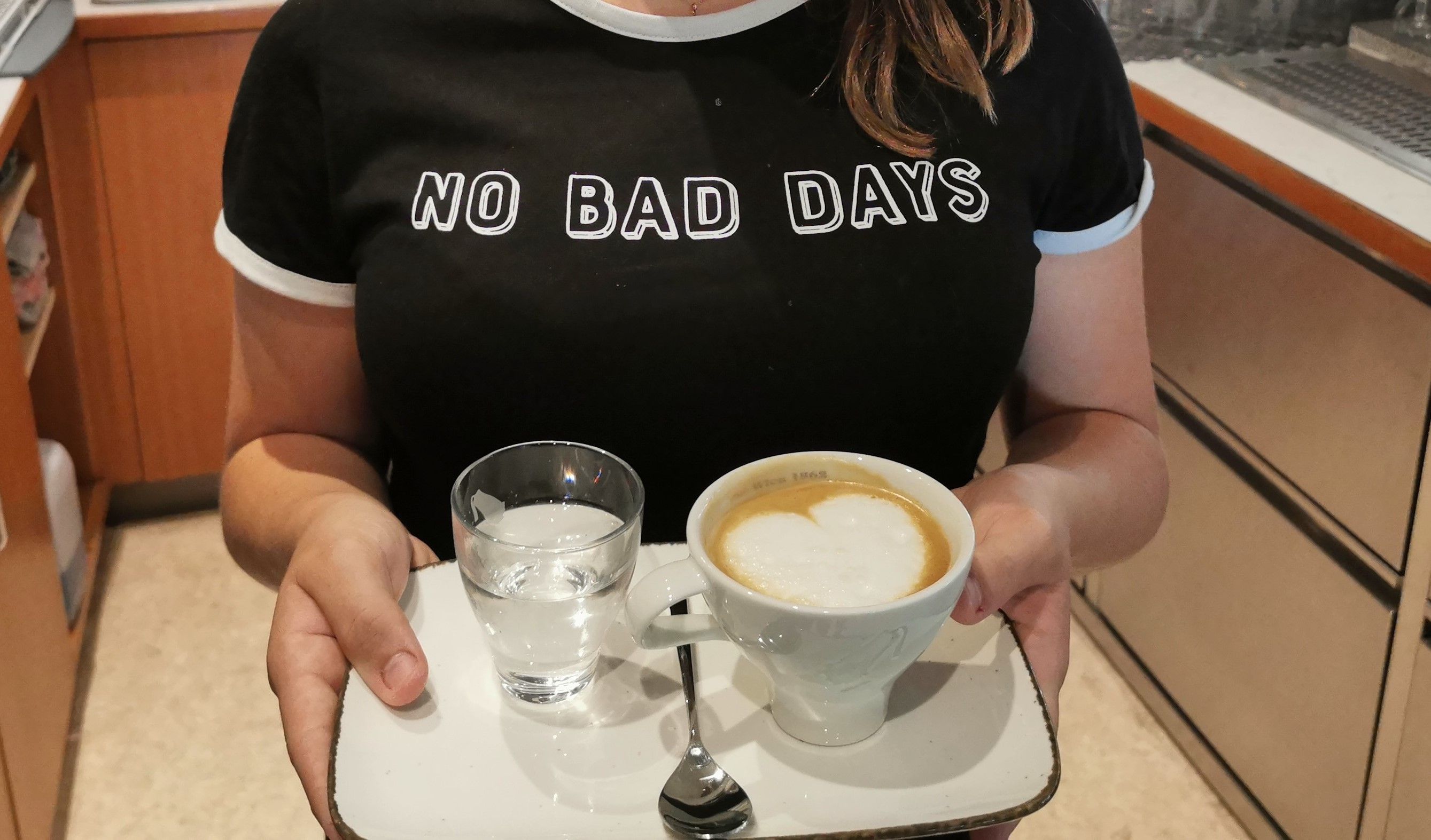 Person holds a tray with a cappuccino and a glass of water.
