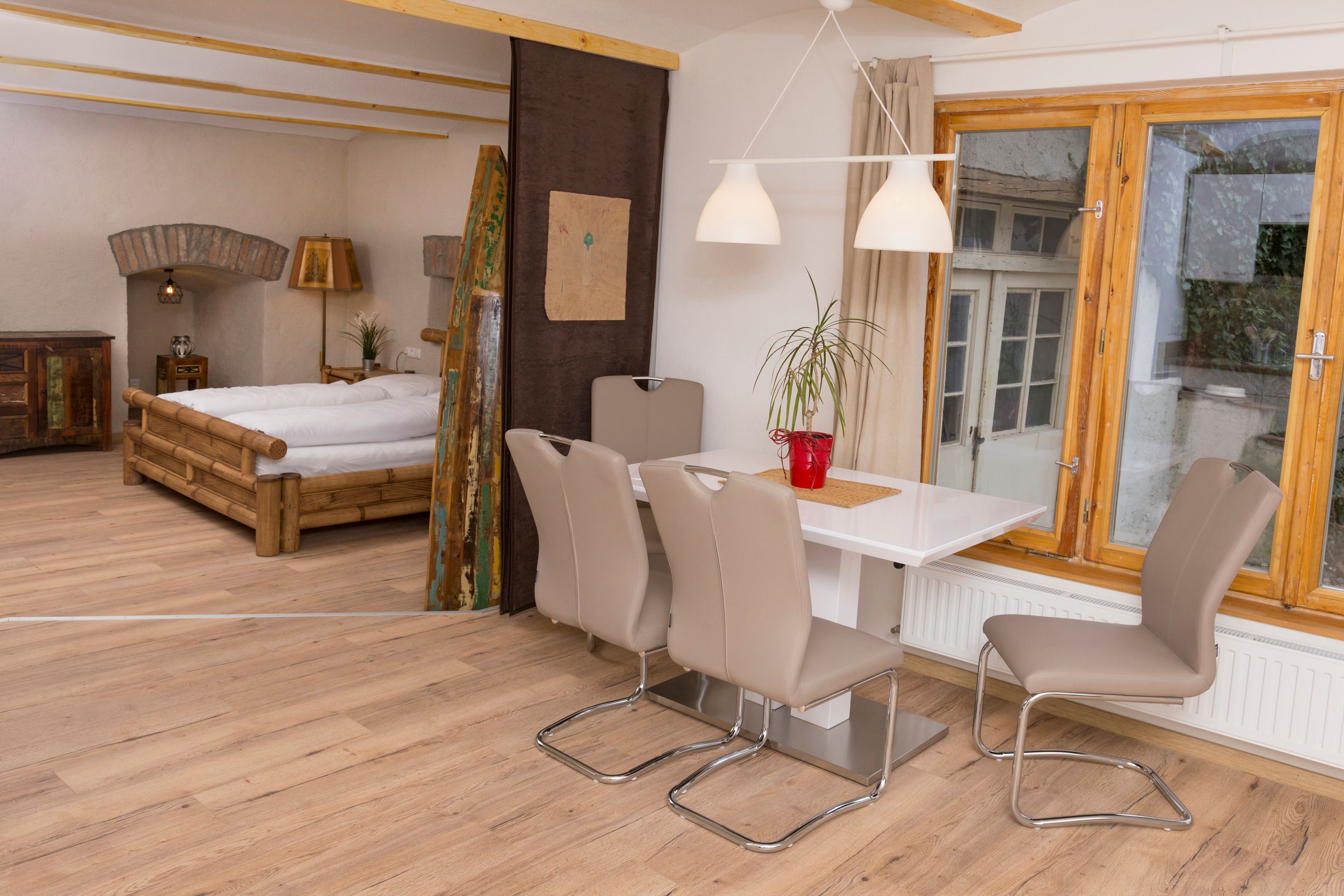 Interior view of a vacation apartment with dining table, chairs, bed and window.