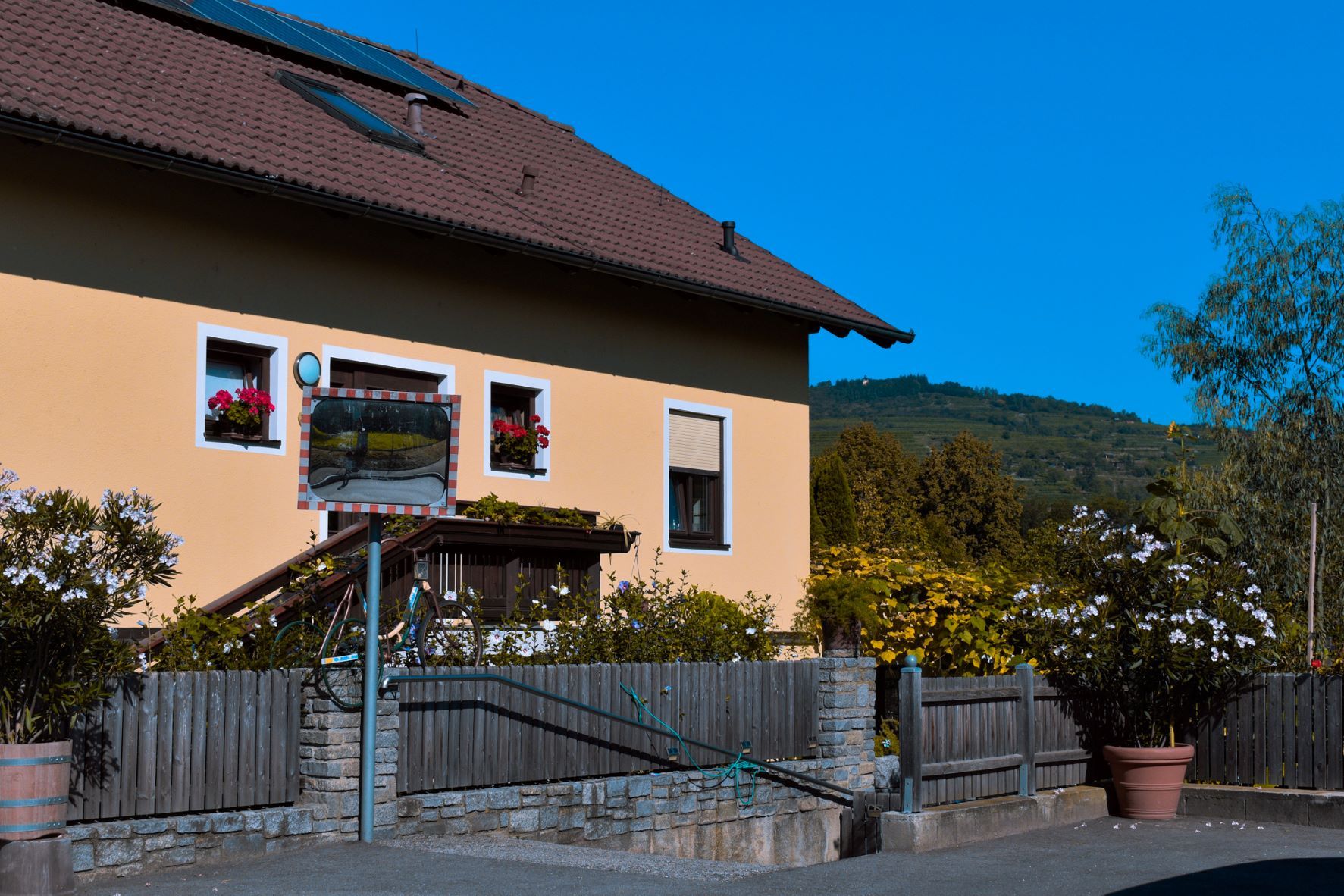 Exterior view of a house with a yellow façade, flowers in the windows and a traffic mirror in the foreground.