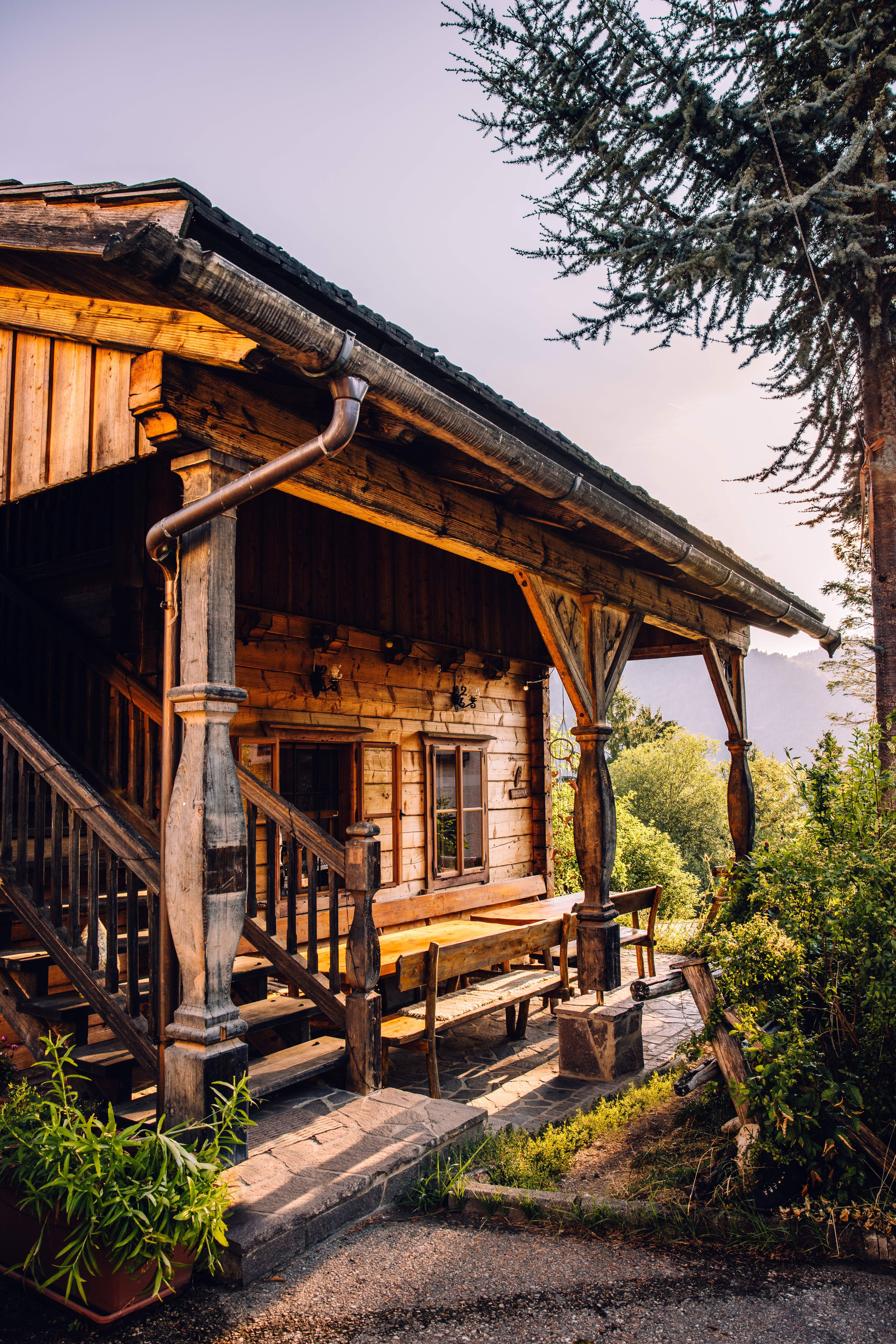 A mountain hut in Opponitz with a covered wooden deck, benches, and a table, surrounded by lush greenery.