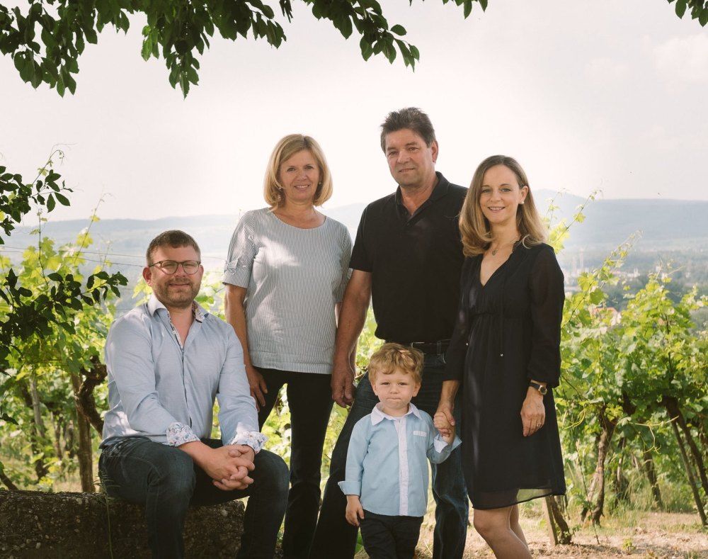Five people pose in a vineyard, including a child. Hills and vines can be seen in the background.