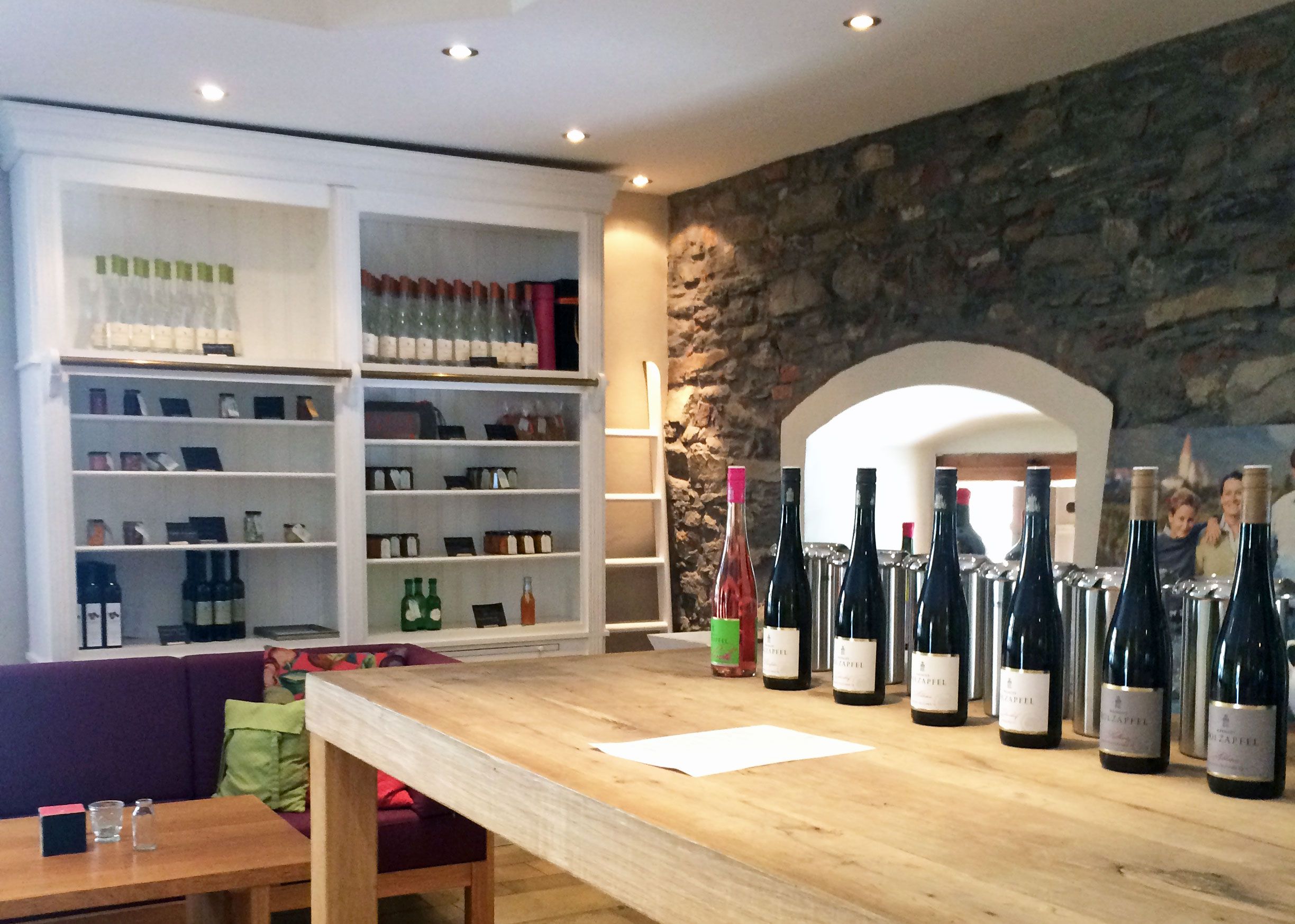 Tasting room with wine bottles on a wooden table and shelves in the background.