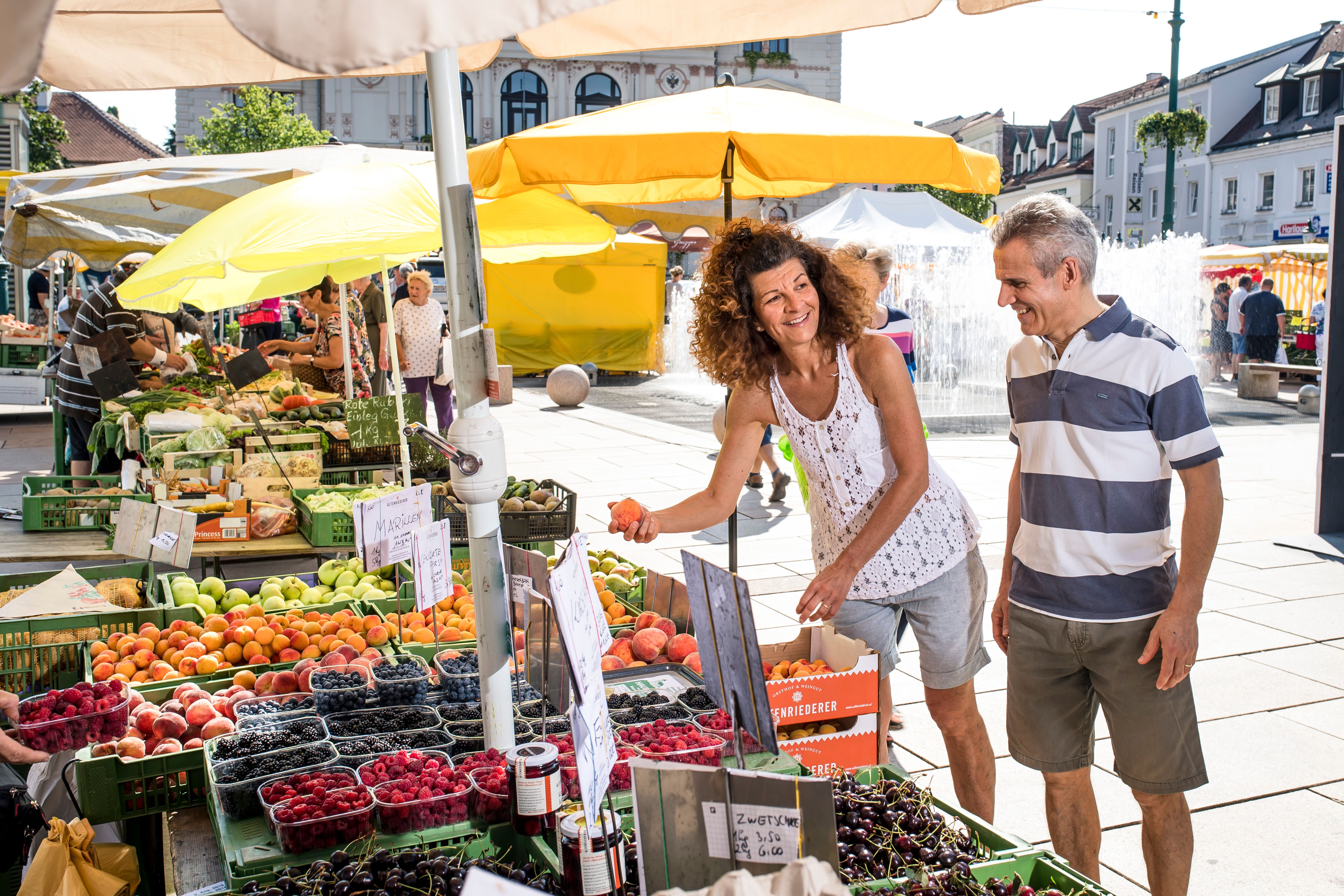 People buy fruit at a market with yellow parasols.