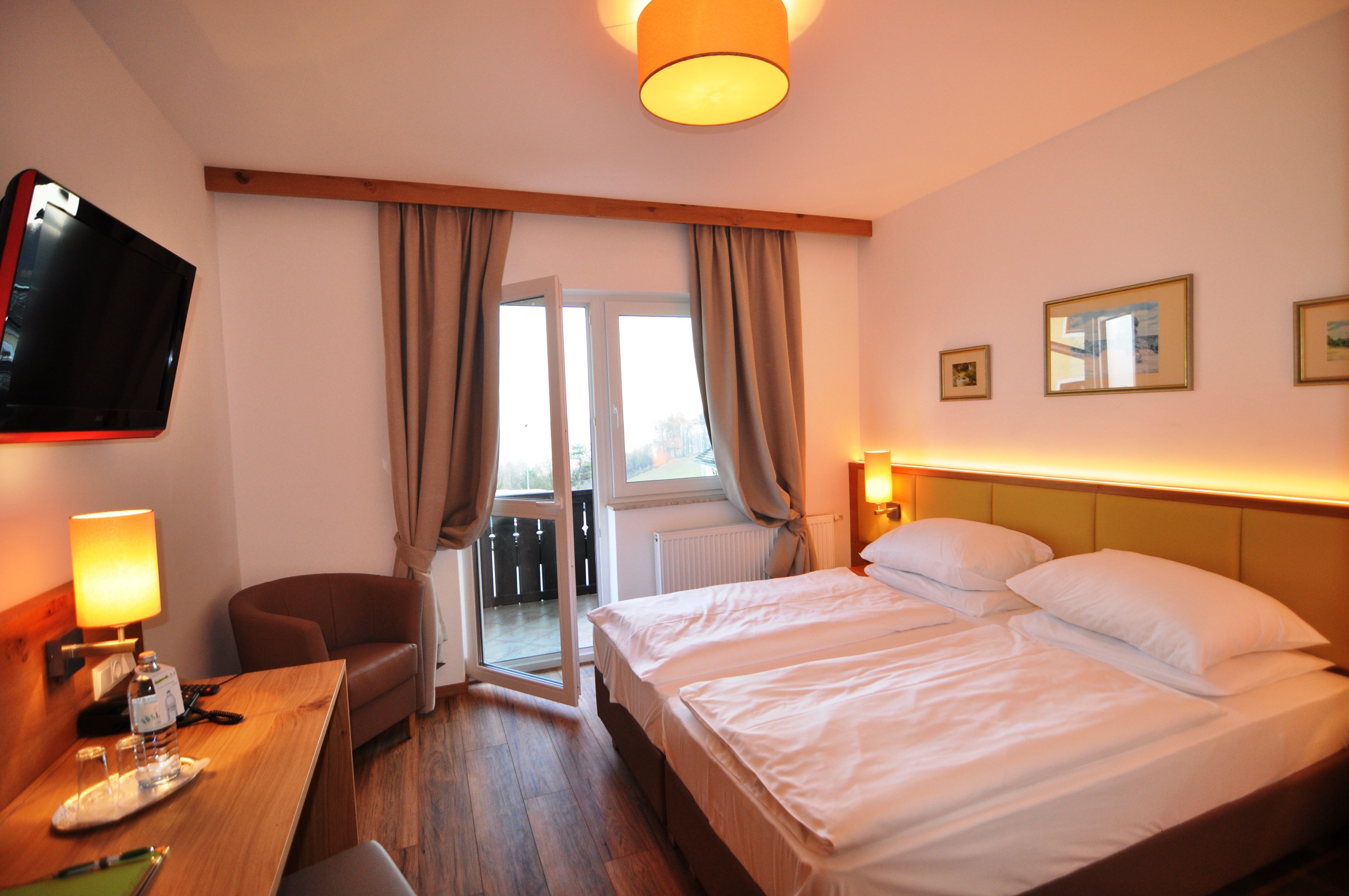 Hotel room with double bed, TV, desk and open balcony window.