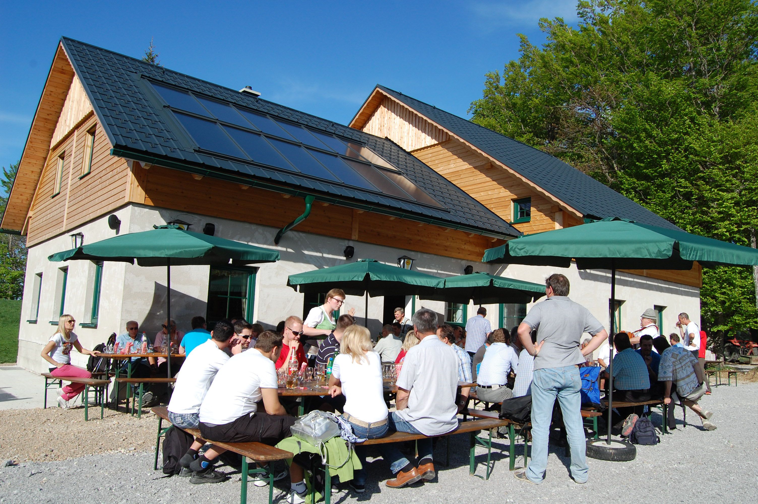 People sit at tables in front of a hut with solar panels and parasols.