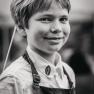 A boy in an apron labeled "Adam-Mühle" smiles at the camera.