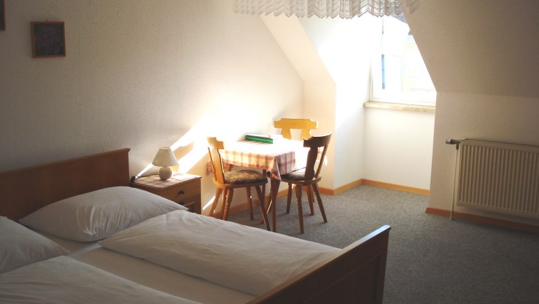 A simply furnished room with bed, table, chairs and window.