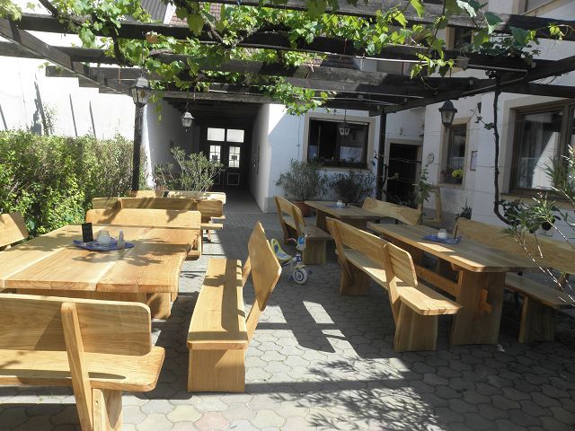 Wooden terrace with tables and benches under a pergola with vines.