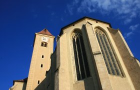View of the Church of the Holy Blood in Pulkau with tower and Gothic windows against a blue sky.