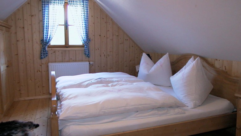 Cozy bedroom with wooden walls, a double bed and a window with blue checkered curtains.
