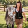 Claudia Langthaler leads a pony in a meadow, with a wooden fence in the background.