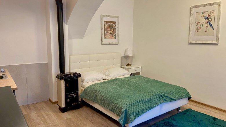 A cozy bedroom with a white bed, green ceiling, carpet and two pictures on the wall.