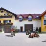 Children play on Kettcars in front of a yellow farm with flower balconies.