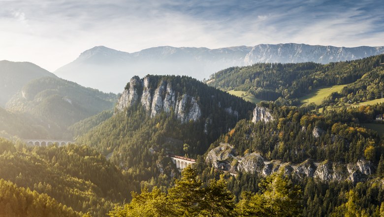 Panoramic view of a mountain landscape with viaduct and wooded hills.