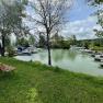 A quiet harbor with several boats, surrounded by green trees and a meadow with a bench.