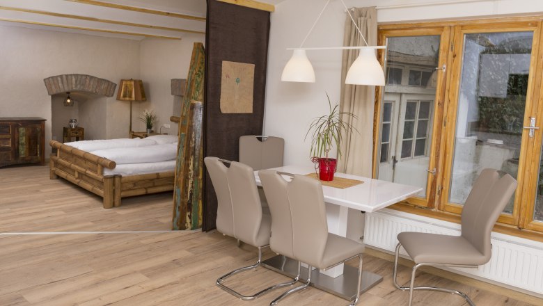 Interior view of a vacation apartment with dining table, chairs, bed and window.