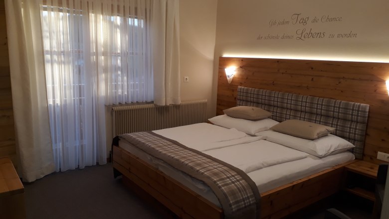 Cozy bedroom with double bed, wooden wall and curtains.