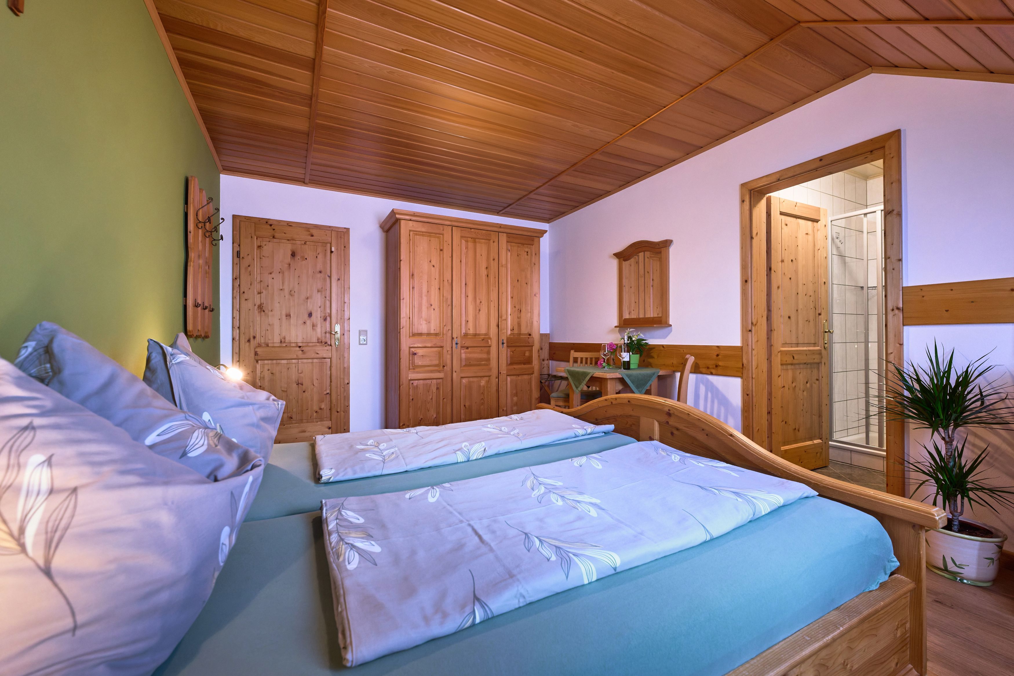 Cozy bedroom with wooden furniture, double bed, closet and small table. A door leads to a bathroom.