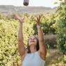 Woman throws wine bottle into the air in a vineyard.