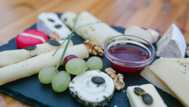 Cheese platter with grapes, nuts and dip on a slate plate.