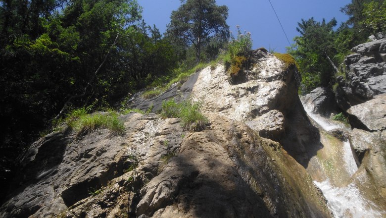 Rocky waterfall with trees and blue sky.