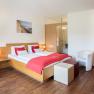 Modern hotel room with double bed, red accents, desk and TV.