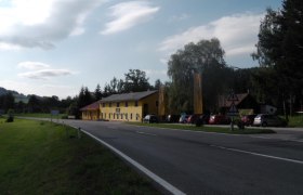 A yellow building on a country road with parked cars and trees in the background.