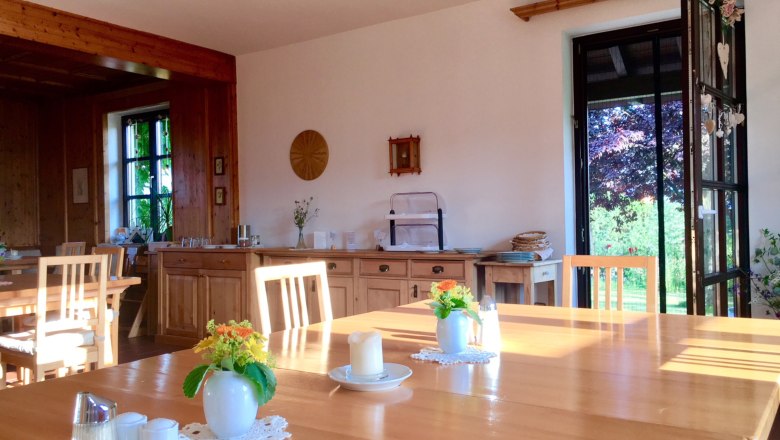A cozy breakfast room with wooden furniture, flowers on the tables and an open door to the garden.