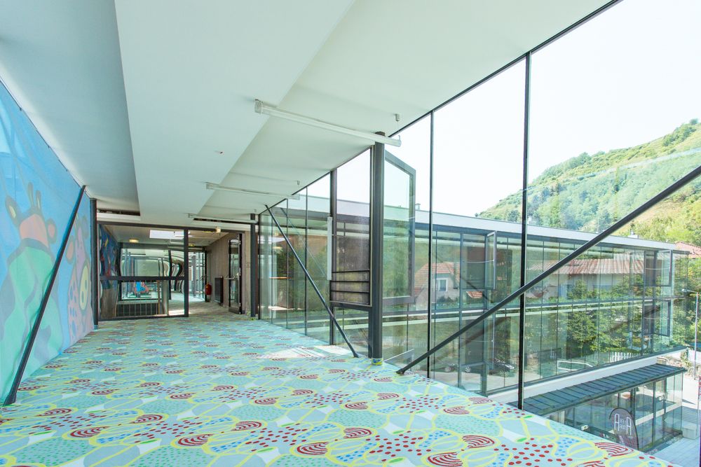 Modern, glazed passageway with colorful carpet and wall art.