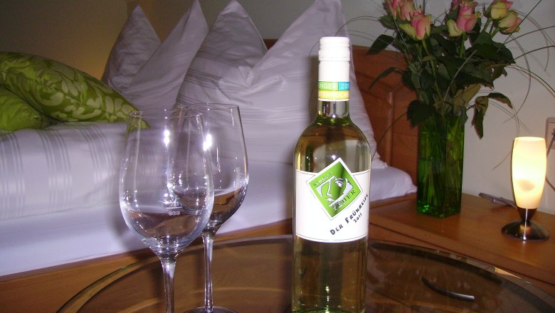 A cozy guest room with a bottle of wine, two glasses and a bouquet of flowers on a table.