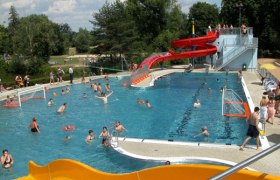 An outdoor pool with a water slide and people playing.