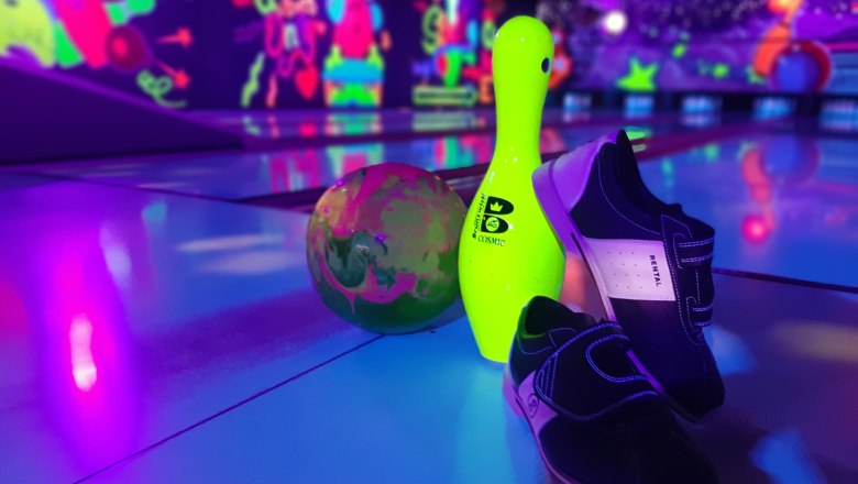 Bowling ball, pins and shoes on a bowling alley with neon-colored lighting.