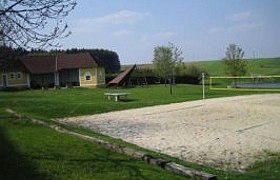Recreational area with volleyball court, meadow and buildings.