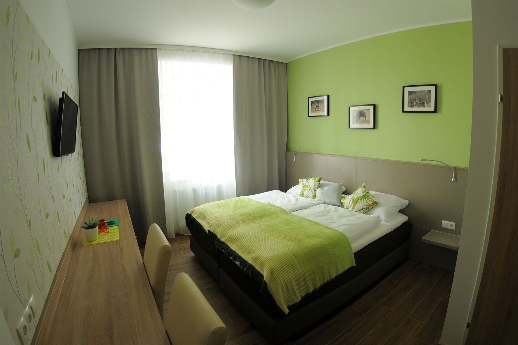Modern guest room with green color scheme, double bed, desk and wall decorations.