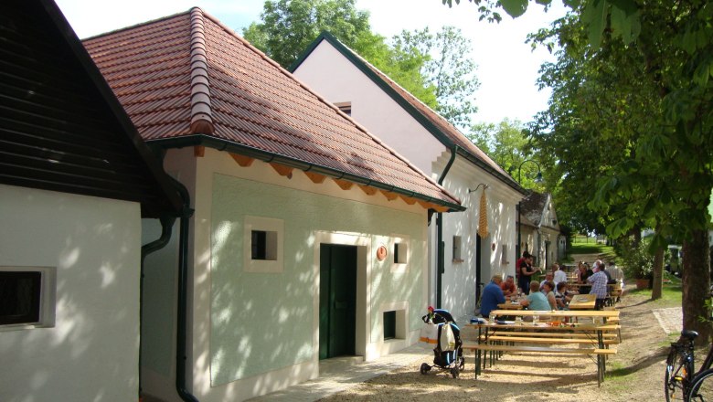 People sit at tables in front of traditional buildings with red roofs.