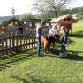 Children stroking a pony in a meadow next to a wooden fence.