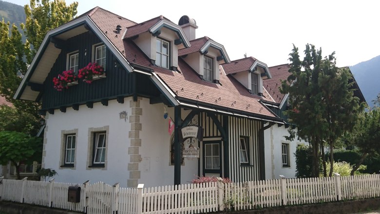 A traditional country house with wooden cladding, red roof tiles and flower boxes in front of the windows. A white wooden fence surrounds the property.